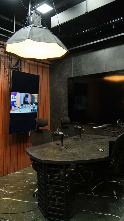 Estúdio da HLS com mesa de gravação, painel de madeira e telas de cenário